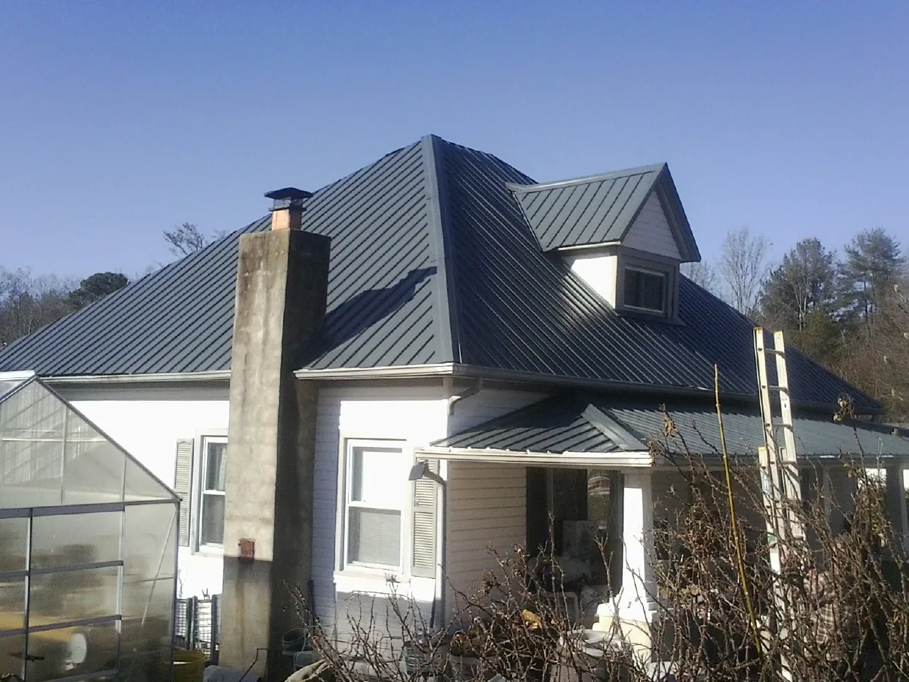Dark blue standing seam metal roof on a white farmhouse with dormer — Slate & Tile Roof Repair by Roofing Brothers in Simonton