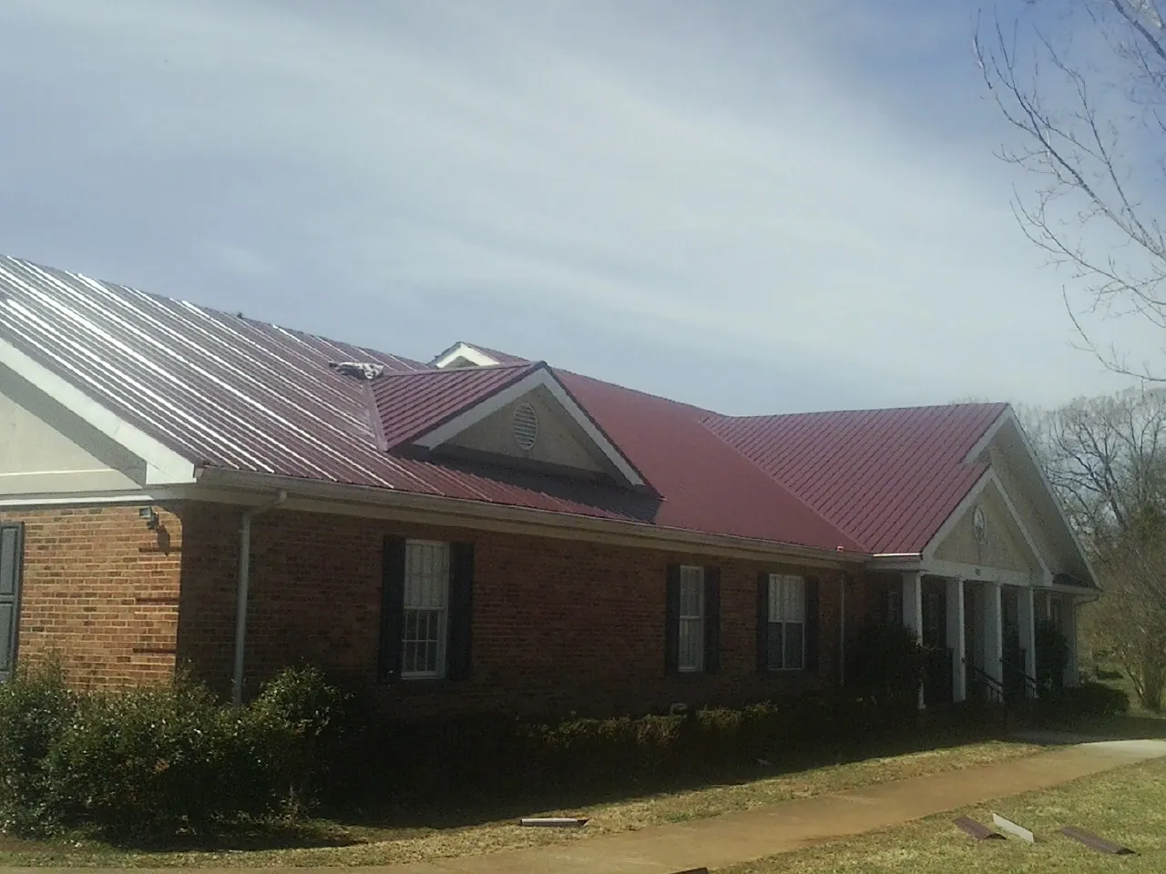 Red metal roof with gabled entries on a long brick building, from a Hail Damage Roof Repair job in Simonton