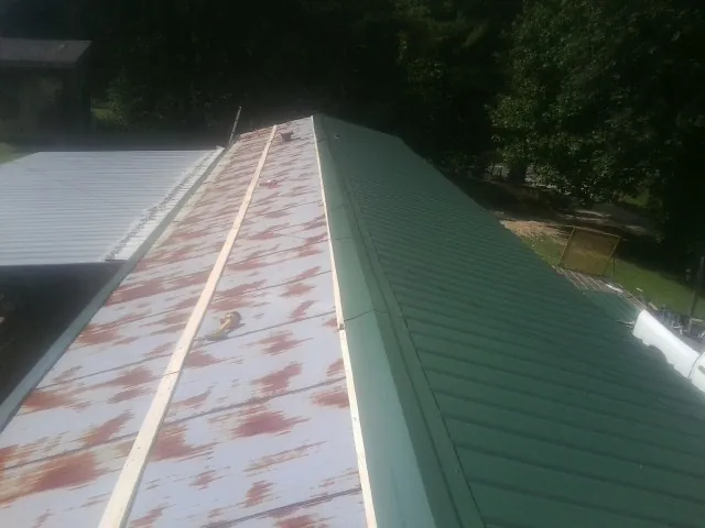 Old rusted panels beside newly installed green metal roofing — Wind Damage Roof Repair by Roofing Brothers in Simonton