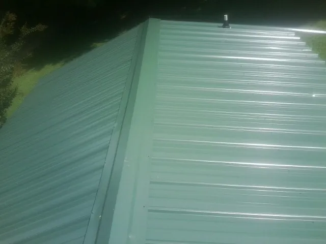 New green metal panels meeting at the ridge of a roof — Flat Roof Repair work by our crew in Simonton