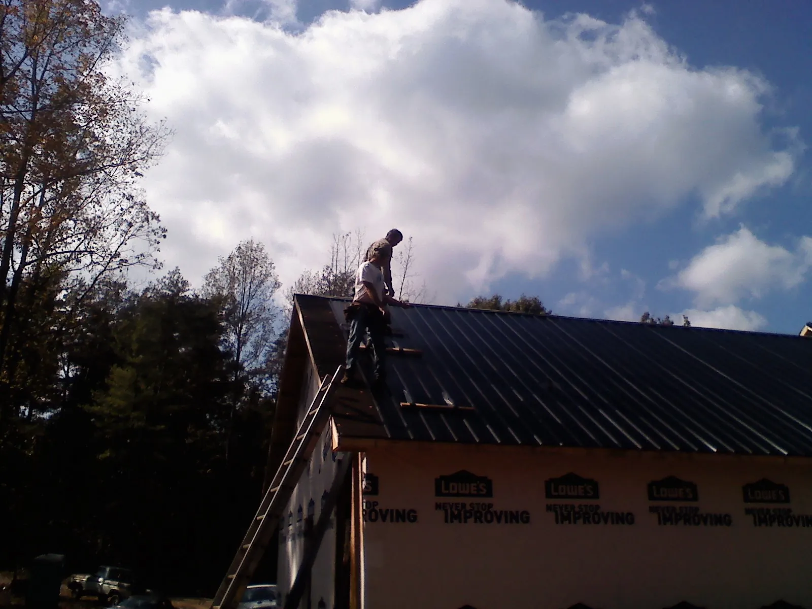 Roofer fastening dark metal panels high against a cloudy sky, from a Roof Inspection job in Simonton